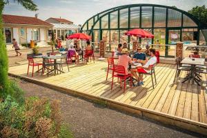 Un grupo de personas sentadas en mesas en una terraza de madera. en Camping 4 étoiles - Parc aquatique - eeiaia, en Olonne-sur-Mer