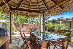 a patio with a glass table and chairs under a straw umbrella at Cape Byron Suite 5 Private Suite with Ensuite in Byron Bay