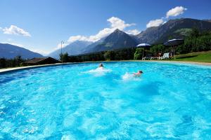 dwie osoby pływające w basenie z górami w tle w obiekcie Pension Laurin w mieście Schenna