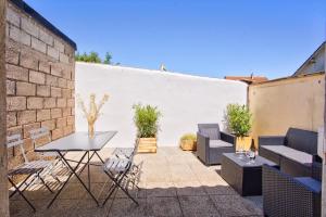 a patio with chairs and tables and a white wall at L'atypique, avec terrasse à 150M de la plage in Lion-sur-Mer