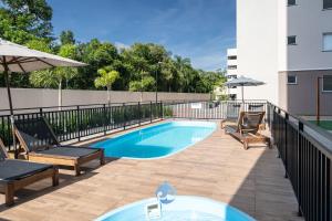 a swimming pool with two chairs and an umbrella at Apartamentos em Bal Piçarras 150 M DA PRAIA com Sacada Wi Fi, Piscina, Portaria 24h, Playground e vaga de GARAGEM in Piçarras