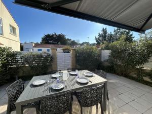 a table with chairs and plates on a patio at Maison de Vacances avec Terrasse Dallée, 6 Couchages, à Deux Pas de l'Océan à St-Jean-de-Monts - FR-1-224C-94 in Saint-Jean-de-Monts