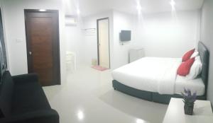 a white bedroom with a bed and a black chair at The Clover Lampang in Lampang