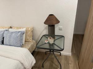 a lamp on a glass table next to a bed at Quarto aconchegante in Amadora