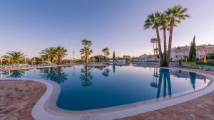 a large swimming pool with palm trees and houses at Apartamento Golden Sky in Cabanas de Tavira