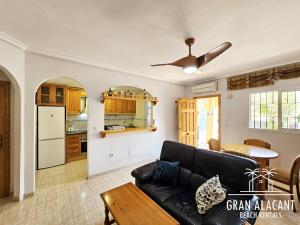 ein Wohnzimmer mit einer schwarzen Couch und einer Küche in der Unterkunft Adosado familiar Novamar 33 in Santa Pola