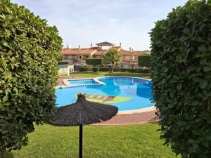 ein großer Pool mit einem Strohschirm im Gras in der Unterkunft Adosado familiar Novamar 33 in Santa Pola