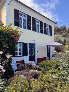 a white house with black shutters and two chairs in a garden at Quinta das Hortênsias in Arco de São Jorge