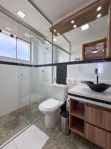 Un baño con inodoro y ducha de cristal. en Apt Pé na Areia - Praia Martim de Sá - Espaço Gourmet na Varanda e Piscina, en Caraguatatuba