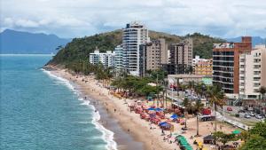una playa con gente y sombrillas y el océano en Apt Pé na Areia - Praia Martim de Sá - Espaço Gourmet na Varanda e Piscina, en Caraguatatuba
