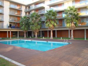 a swimming pool in front of a building with palm trees at Apartamento Playa Esquirol in Cambrils