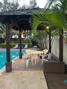 a wooden pergola with a table and chairs next to a pool at Anaya Résidence in Flic-en-Flac