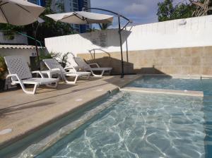 a swimming pool with chairs and an umbrella at Apartamentos Villa Leonor in Coveñas