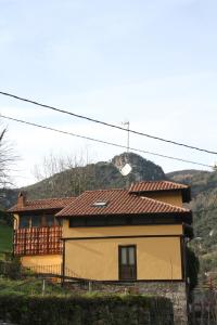 uma casa amarela com uma montanha ao fundo em Ca María Fayas em Proaza