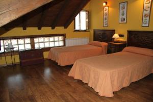 two beds in a room with yellow walls and wooden floors at Ca María Fayas in Proaza