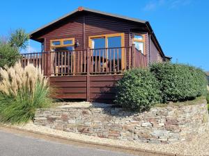 a log cabin with a balcony and a stone wall at Laurel Lodge in Tintagel