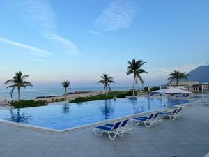 a swimming pool with chairs and palm trees and the ocean at Sifah Seascape House in Muscat