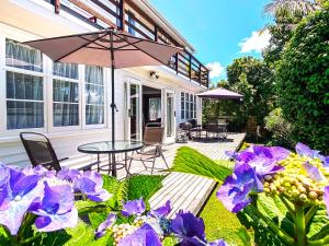 a patio with a table and umbrella and purple flowers at Bavaria Boutique Hotel in Auckland