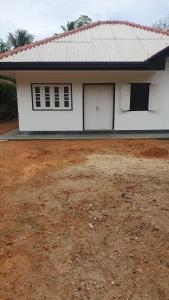 a white house with two windows and a dirt yard at Madiha Sampath Surf Villa in Matara