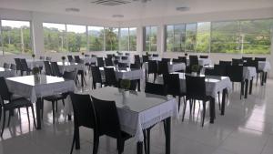 uma sala de jantar com mesas e cadeiras brancas e janelas em France Hotel em Guarabira