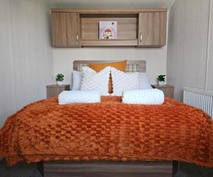 a bed with an orange blanket and white pillows at Holiday Home at Combe Haven, St Leonards, Hastings in St. Leonards