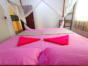 two beds in a room with pink sheets and red pillows at vihanga homestay in Mirissa