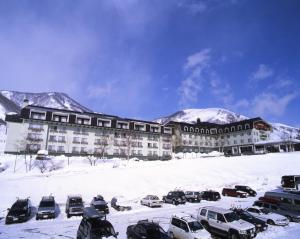un grand bâtiment avec des voitures garées dans la neige dans l'établissement Hakuba Alps Hotel, à Otari