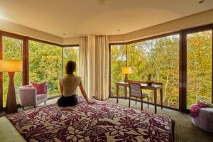 una mujer sentada en una cama en una habitación con ventanas en Hotel Zochova Chata - Adult friendly, en Modra