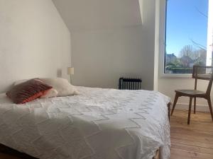 ein weißes Bett in einem Zimmer mit Fenster in der Unterkunft Maison cosy in Larmor-Baden