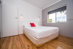 a white bedroom with a large bed with a red pillow at Lakeside Cabins & Holiday Village in Sussex inlet +27 photos