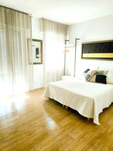 a white bedroom with a large bed and wooden floors at Appartamento "Laghetto 1" con tre camere e bagni privati cucina in condivisione in Castel San Pietro Terme