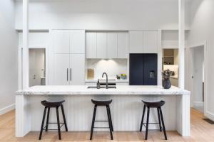a kitchen with white cabinets and bar stools at Luxury Central Villa with Spa Pool Prime Location in Auckland