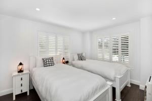 two beds in a bedroom with white walls and windows at Margaret's Hamptons Beach House in Hawks Nest