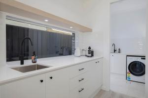 a white kitchen with a sink and a dishwasher at Shoreline Luxe - Refined Beachside Elegance with Spa in Caves Beach +32 photos