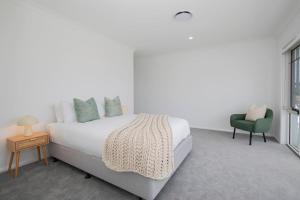 a white bedroom with a bed and a green chair at Shoreline Luxe - Refined Beachside Elegance with Spa in Caves Beach