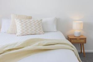 a bedroom with a white bed and a table with a lamp at Shoreline Luxe - Refined Beachside Elegance with Spa in Caves Beach