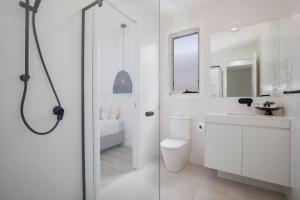 a white bathroom with a toilet and a sink at Shoreline Luxe - Refined Beachside Elegance with Spa in Caves Beach