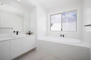a white bathroom with a tub and a window at Shoreline Luxe - Refined Beachside Elegance with Spa in Caves Beach