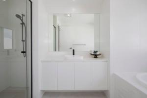 a white bathroom with a sink and a mirror at Shoreline Luxe - Refined Beachside Elegance with Spa in Caves Beach
