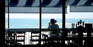 a woman sitting at a table looking out at the ocean at Prima Tel Aviv Hotel in Tel Aviv