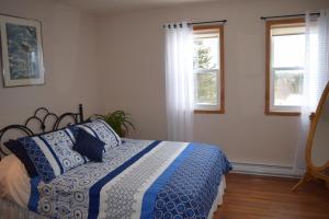- une chambre avec un lit bleu et blanc et 2 fenêtres dans l'établissement Gîte Aux Jardins De L'Anse, à Percé