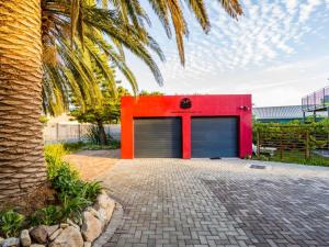 a red building with two garage doors next to a palm tree at Two Palm House - Vermont Hermanus in Hermanus