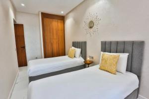 two beds in a hotel room with white and yellow pillows at KH APPARTEMENT appart1 in Essaouira