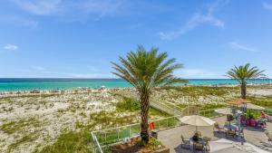 a beach with a palm tree and chairs and the ocean at Beach Club Gulf Front 3B Condo - 2004 in Pensacola Beach