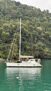 a white boat in the water next to a mountain at Aventura náutica em Paraty hospedagem flutuante na cidade Veleiro Maverick in Paraty