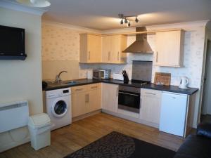 a kitchen with white cabinets and a washer and dryer at Coasters Holiday Flats in Macduff