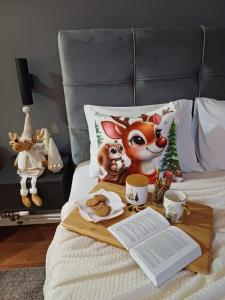 a bed with a tray with a mickey mouse and a table with a book at Alex lux apartman in Kragujevac
