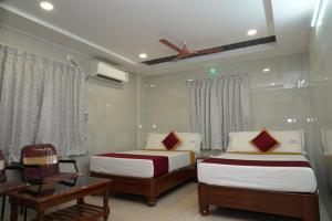a bedroom with two beds and a table and a fan at HOTEL THANVI iNN in Guntūr
