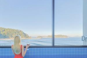 Eine Frau, die ein Glas Wein mit Blick auf den Ozean hält. in der Unterkunft Geoje Dream Angel Pool Villa in Geoje