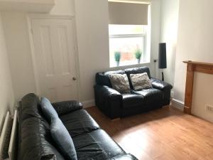 a living room with a black leather couch and a window at Ormskirk lets in Ormskirk